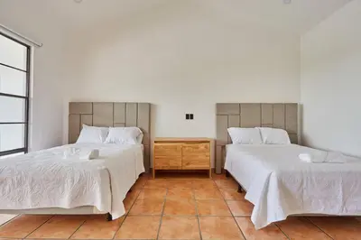 a bedroom with two beds with white sheets and a wooden table at New in the heart of the city 5 min to US Embassy in Nuevo Cuscatlán