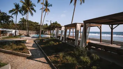 a beach with benches and palm trees and the ocean at Coco Surf Tropical Village in La Libertad
