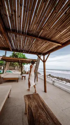 a woman in a white dress walking under a wooden umbrella at Coco Surf Tropical Village in La Libertad