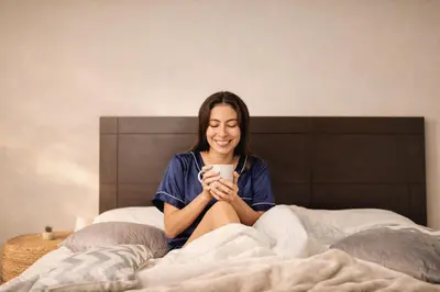 a woman sitting on a bed holding a cup of coffee at Habitación Deluxe Aire - Villa Valle Campo in Nahuizalco